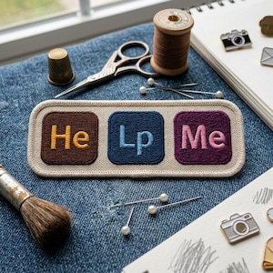 May include: Embroidered patch with the words "He Lp Me" in a periodic table style. The patch is brown, blue, and purple with a cream border. Sewing notions, including scissors, pins, and thread, are arranged around the patch on a denim surface.