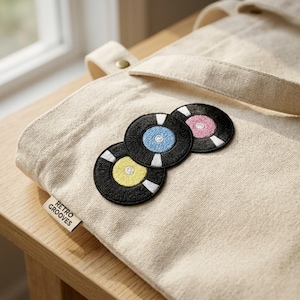 May include: Beige canvas tote bag with three embroidered vinyl record patches. The patches have black backgrounds with white stripes and colored centers: yellow, blue, and pink. A small tag reads "Retro Grooves".