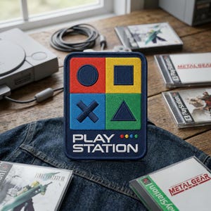 May include: A rectangular patch with the words "PLAY STATION" in white, featuring a colorful design of a circle, square, X, and triangle. The patch is on a denim jacket, with PlayStation game cases and a console in the background.
