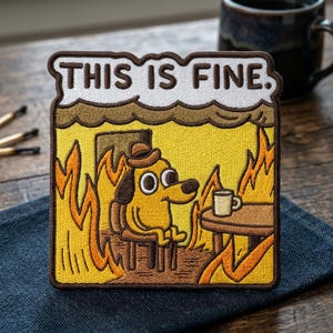 May include: Embroidered patch featuring a cartoon dog in a burning room, wearing a hat and sitting in a chair. The patch has the text "THIS IS FINE" above the dog. The dog is holding a coffee cup.