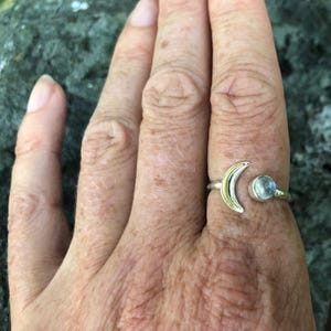 May include: A silver ring with a crescent moon design and a clear gemstone. The moon is accented with gold.