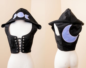 Könnte beinhalten: Schwarze Kapuzenweste mit einem lila Mond- und Dreimond-Design. Die Weste hat einen Schnürverschluss vorne und ist ärmellos.