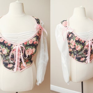 May include: A black and white floral print corset top with pink ribbon ties and white sheer long sleeves.