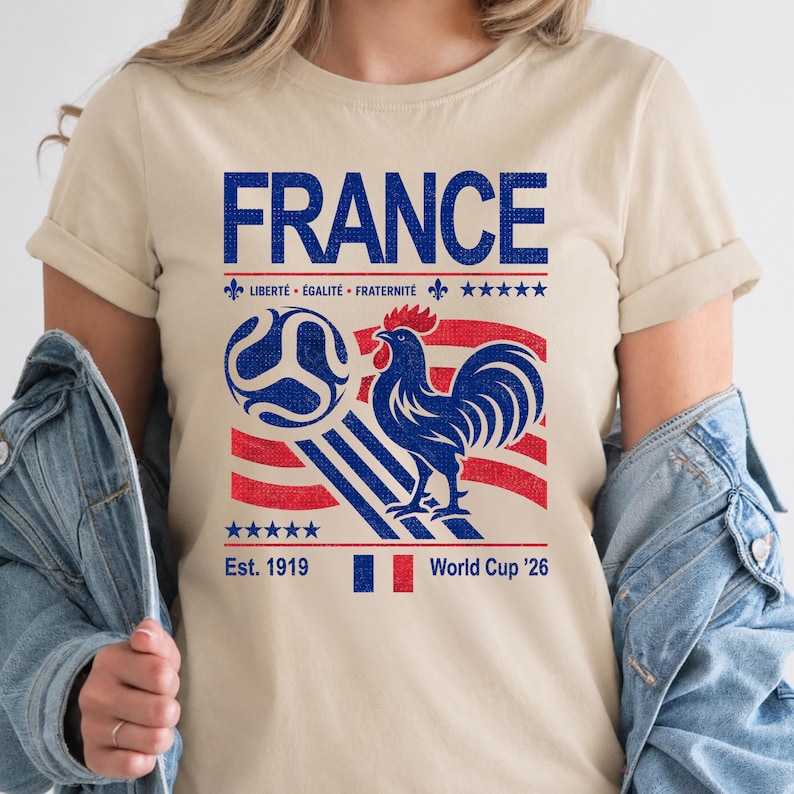 May include: Beige t-shirt with a blue and red graphic featuring the word "FRANCE", a soccer ball, a rooster, and the text "Est. 1919" and "World Cup '26". The shirt also has the French motto "Libert&eacute;, &Eacute;galit&eacute;, Fraternit&eacute;".
