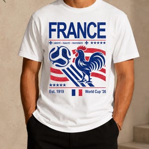 May include: White t-shirt with a graphic design featuring the word "FRANCE" in blue, a blue rooster, and a soccer ball. The design includes the text "Libert&eacute;, &Eacute;galit&eacute;, Fraternit&eacute;", stars, and "World Cup '26".