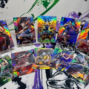 Puede incluir: Una colección de cartas coleccionables holográficas con personajes de anime en poses de acción. Las cartas muestran colores vibrantes y nombres de personajes, con un acabado brillante e iridiscente. Cada carta se exhibe en un soporte transparente.
