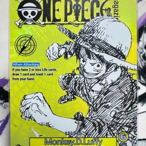 May include: A One Piece trading card featuring a black and white illustration of Monkey D. Luffy in action. The card has a yellow background with Japanese text and English text that reads "When Attacking" and "Monkey.D.Luffy".