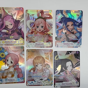May include: Six One Piece trading cards featuring anime-style female characters Jewelry Bonney, Shirahoshi, Nefeltari Vivi, Rebecca, Nami, and Boa Hancock. Each card displays a 5000 power level, character names, and game text in a holographic finish.