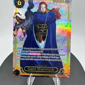 May include: A holographic trading card featuring Saint Shamrock, a character with long reddish hair wearing a dark blue cloak over black armor. A dark, shadowy creature is positioned to the left. The card displays text, a power level of 9000, and game mechanics.