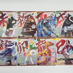 May include: A collection of twelve One Piece trading cards arranged in two rows. Each card features a unique anime character illustration, bold red Japanese kanji characters, numerical power stats, and descriptive text in English.