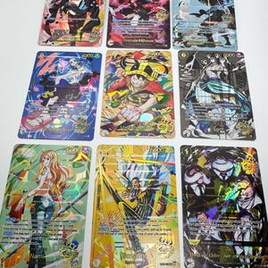 May include: A collection of nine One Piece trading cards arranged in a three-by-three grid. Each card features colorful anime-style character illustrations, including Shanks, Dracule Mihawk, Edward Newgate, Nefertari Vivi, Monkey D. Luffy, Enel, Nami, Borsalino, and The Five Elders.