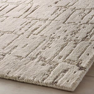 May include: A rectangular area rug featuring a high-low pile construction with a textured, geometric pattern of raised off-white blocks and recessed light brown channels, creating a dimensional surface with a soft, dense, and tufted appearance.