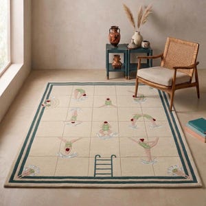 May include: A rectangular area rug featuring a cream-colored background with a grid pattern resembling a swimming pool. The rug displays embroidered figures of swimmers in green swimsuits, a dark teal border, and a dark teal pool ladder graphic.