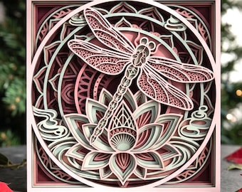 May include: A square multi-layered wooden wall art piece featuring a central dragonfly hovering above a lotus flower. The design uses a palette of soft pink, sage green, and deep burgundy, with intricate laser-cut geometric patterns and circular frames.
