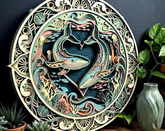 May include: A circular multi-layered wooden wall art piece featuring two whales forming a heart shape in the centre. The design includes intricate cutouts of waves, coral, seashells, and small fish in shades of teal, peach, cream, and dark blue.