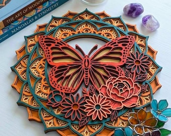 May include: A multi-layered wooden mandala wall art piece featuring a central butterfly and floral design in shades of orange, teal, and red. The circular artwork is displayed alongside a candle, two purple stones, and small stained glass flowers.