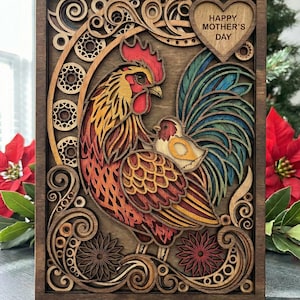 May include: A layered wooden artwork featuring a rooster and chick, with a heart-shaped element that reads "Happy Mother's Day." The rooster has red, orange, and yellow feathers, and the chick is nestled on its back. The artwork is framed in dark brown wood.