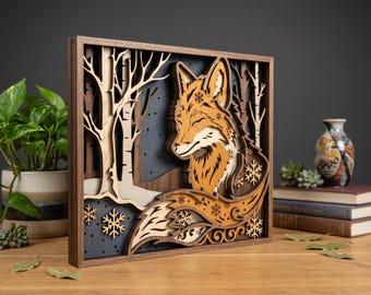 May include: A layered wooden art piece featuring a fox in a winter forest scene. The fox is orange and white, with snowflake details. The background includes trees and a dark blue sky, all within a dark brown frame.