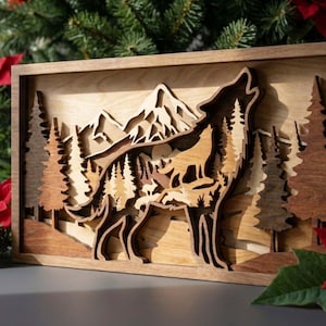 May include: A layered wooden artwork showing a howling wolf in a forest setting. The piece features a wolf silhouette, trees, and mountains, all made from different shades of wood. The artwork is framed in natural wood, creating a three-dimensional effect, with a depth of field.