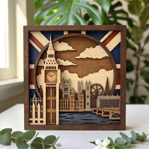 Puede incluir: Una pieza de arte mural cuadrada de madera con un recorte 3D en capas del horizonte de Londres, que incluye el Big Ben con un reloj, el Parlamento y el London Eye, sobre un fondo que representa la bandera Union Jack en azul, rojo y blanco.