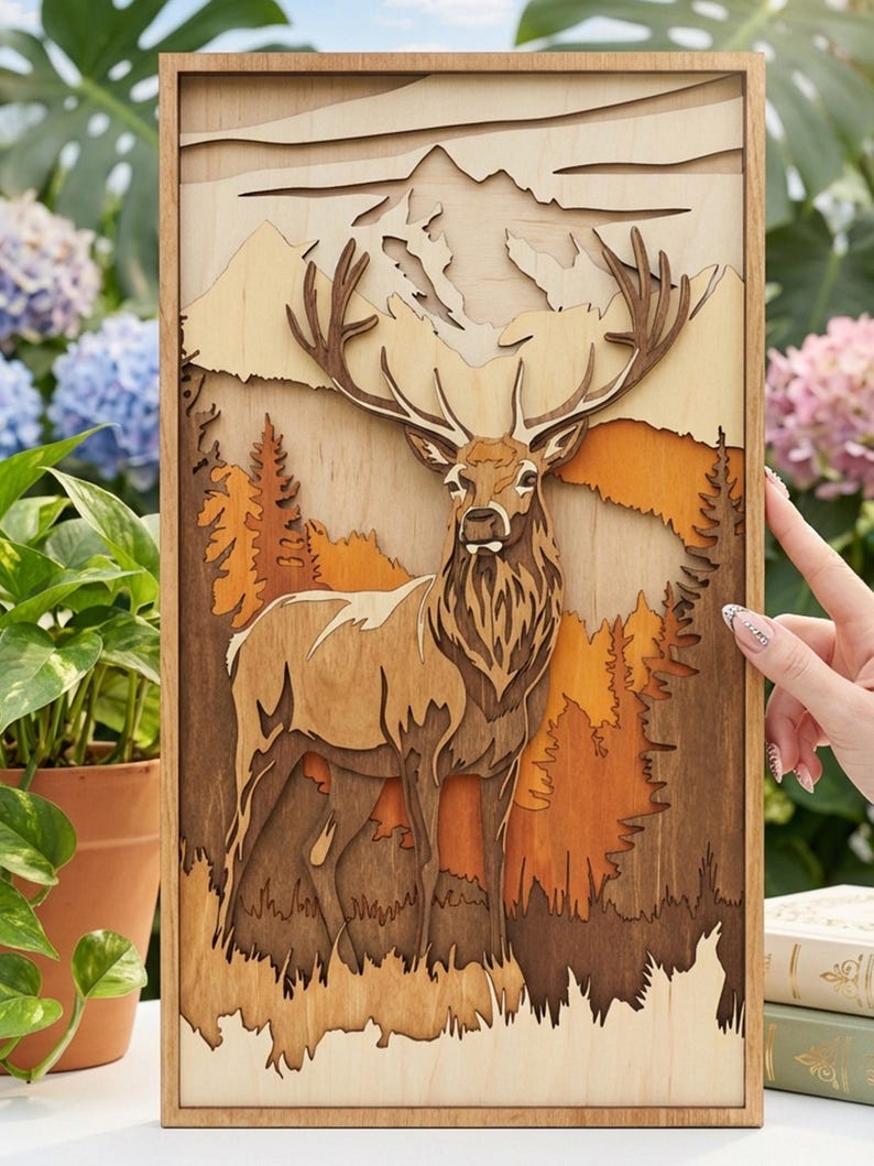 May include: A wooden layered art piece featuring a majestic deer in a forest scene. The artwork uses various shades of brown and orange to depict the deer, trees, and mountains. The piece is framed in a light-colored wood.