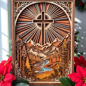 May include: A rectangular multi-layered wooden wall art piece featuring a central cross surrounded by sunburst rays. The scene depicts a landscape with layered mountains, a winding blue river, and pine trees, all framed by an arched border.