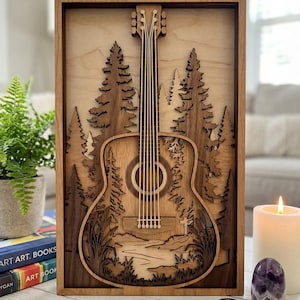 May include: A wooden wall art piece featuring a detailed acoustic guitar design set against a forest landscape. The artwork is crafted from layered wood, showcasing a natural wood grain finish and a rectangular frame. The guitar's strings and soundhole are clearly visible.