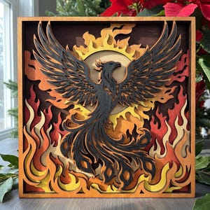 May include: A square wooden wall art piece featuring a multi-layered laser-cut design of a black phoenix rising from flames. The artwork uses shades of yellow, orange, and red to depict fire, set against a dark brown background within a frame.