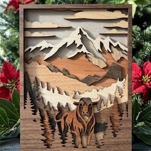 May include: A layered wooden art piece depicting a mountain landscape with a bull in the foreground. The artwork features various shades of brown and tan wood, creating a 3D effect. The bull has large horns and stands in front of a forest.
