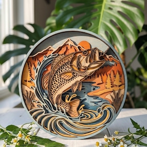 May include: A circular multi-layered wooden wall art piece featuring a jumping bass fish in the center. The design includes a mountain range, a forest of pine trees, and swirling water waves in shades of orange, brown, blue, and cream.