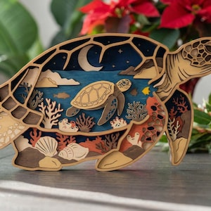May include: A multi-layered wooden art piece shaped like a sea turtle. The design includes a night sky with a moon, ocean, and coral reef. The turtle is brown and tan, with blue and orange accents.