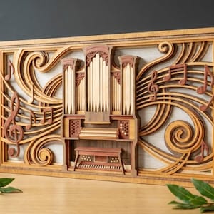 May include: A layered wooden art piece depicting a pipe organ with musical notes and swirling lines. The artwork features a natural wood frame and accents in shades of brown and red. The design is intricate and detailed, showcasing a musical theme.