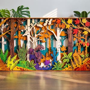 May include: A multi-layered wooden forest scene with trees, foliage, and a variety of colors. The artwork features a mix of trees, including birch and other deciduous trees, with colorful leaves and plants. The piece is rectangular and appears to be a wall hanging.