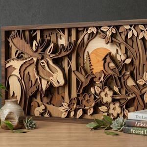 Puede incluir: Una obra de arte de madera multicapa que representa un alce, pájaros y una escena de puesta de sol. La obra utiliza varios tonos de madera marrón y beige, con un marco marrón oscuro. Incluye una ardilla, flores y árboles.