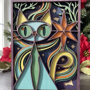 May include: A multi-layered wooden wall art piece featuring a stylised cat with large green eyes, pointed yellow ears, and a light blue body. The design includes an orange star, swirling lines, and small stars against a deep purple background.