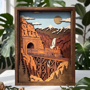 Puede incluir: Una pieza de arte mural de madera multicapa que muestra una locomotora de vapor cruzando un puente de caballetes. La escena representa un tren saliendo de un túnel de montaña, una cascada, picos nevados y un sol en un cielo azul.