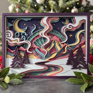 May include: A multi-layered wooden wall art piece featuring a landscape with a mountain, a winding river, and evergreen trees. The scene includes a crescent moon, swirling clouds, and a circular arch with runic symbols in shades of purple, pink, teal, and yellow, all enclosed within a dark purple rectangular frame.