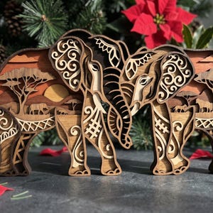 May include: A layered wooden artwork depicting three elephants in a savanna setting. The elephants are intricately cut with decorative patterns. The background shows a sunset with trees and animals. The piece is made of various shades of brown wood.