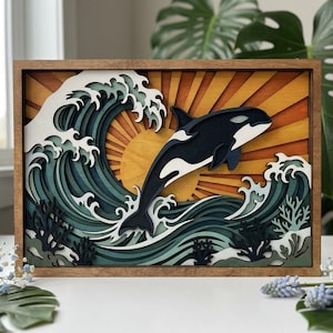 May include: A multi-layered wooden wall art piece featuring a black and white orca jumping through a stylised ocean wave. The background displays a yellow and orange sunburst design, while the foreground includes dark blue coral accents.