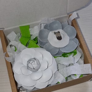 May include: Two white leather flower brooches in a cardboard box with green and white tissue paper. One brooch has a silver clip and the other has a white center.
