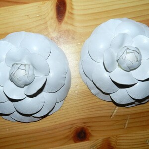 May include: Two white fabric flower brooches with a layered petal design.