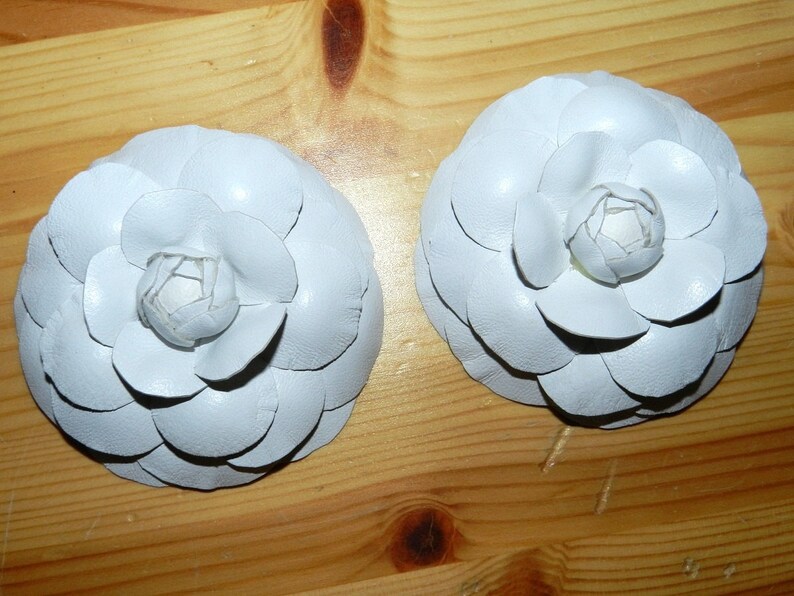 May include: Two white fabric flower brooches with a layered petal design.
