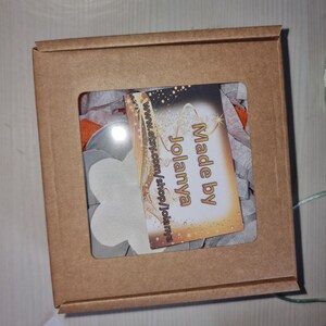 May include: A brown cardboard box with a clear window showing white flower-shaped decorations and a small card that says "Made by Jolanya" and "www.etsy.com/shop/jolanya".