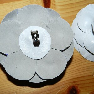 May include: Two white fabric flower brooches with a silver metal clip on the back of one.