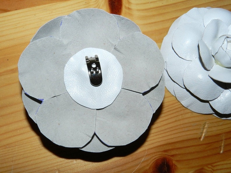 May include: Two white fabric flower brooches with a silver metal clip on the back of one.