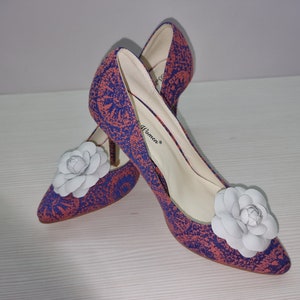 May include: A pair of high-heeled shoes with a floral pattern in shades of pink and blue. The shoes have a white flower embellishment on the toe.