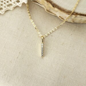 May include: A gold chain necklace featuring a vertical bar pendant. The pendant is set with five small, clear, round-cut stones arranged in a straight line. The delicate chain connects to the top of the slender, polished gold bar setting.