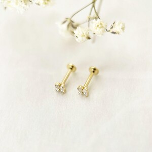 Puede incluir: Un par de pendientes de oro con engaste de cuatro garras, que presentan un grupo de cuatro peque&ntilde;as piedras transparentes dispuestas en forma cuadrada en la cabeza de cada poste, junto a peque&ntilde;as flores blancas.