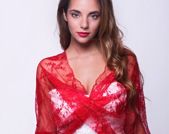 May include: A woman wearing a white dress with a red lace shawl. The shawl is draped over her shoulders and tied at the front. The woman is looking at the camera.