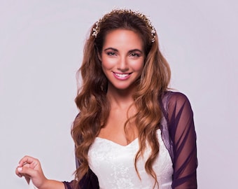 Pode incluir: Uma mulher vestindo um vestido de noiva branco com um xale roxo transparente e uma faixa de cabeça floral.